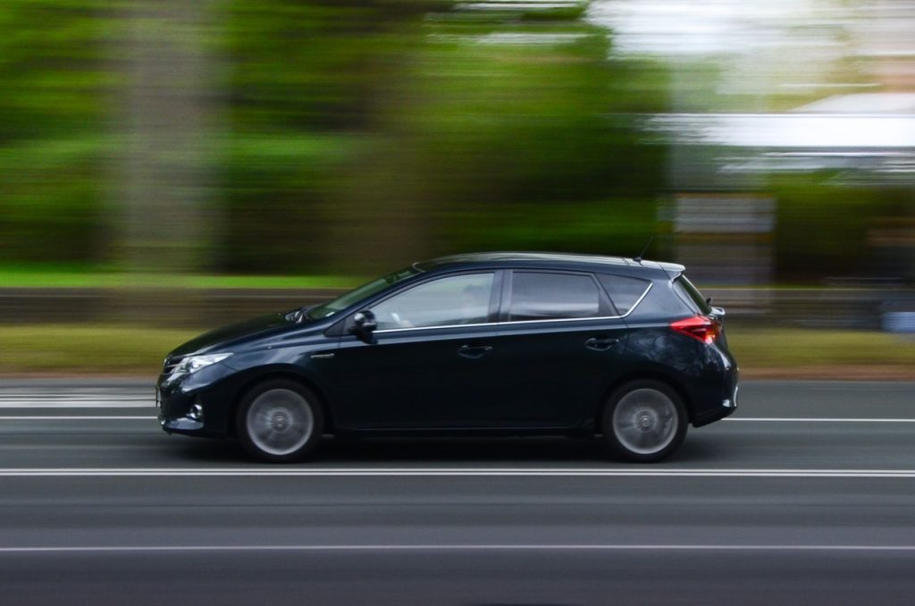 Black car captured in motion blur as it speeds down an urban road.